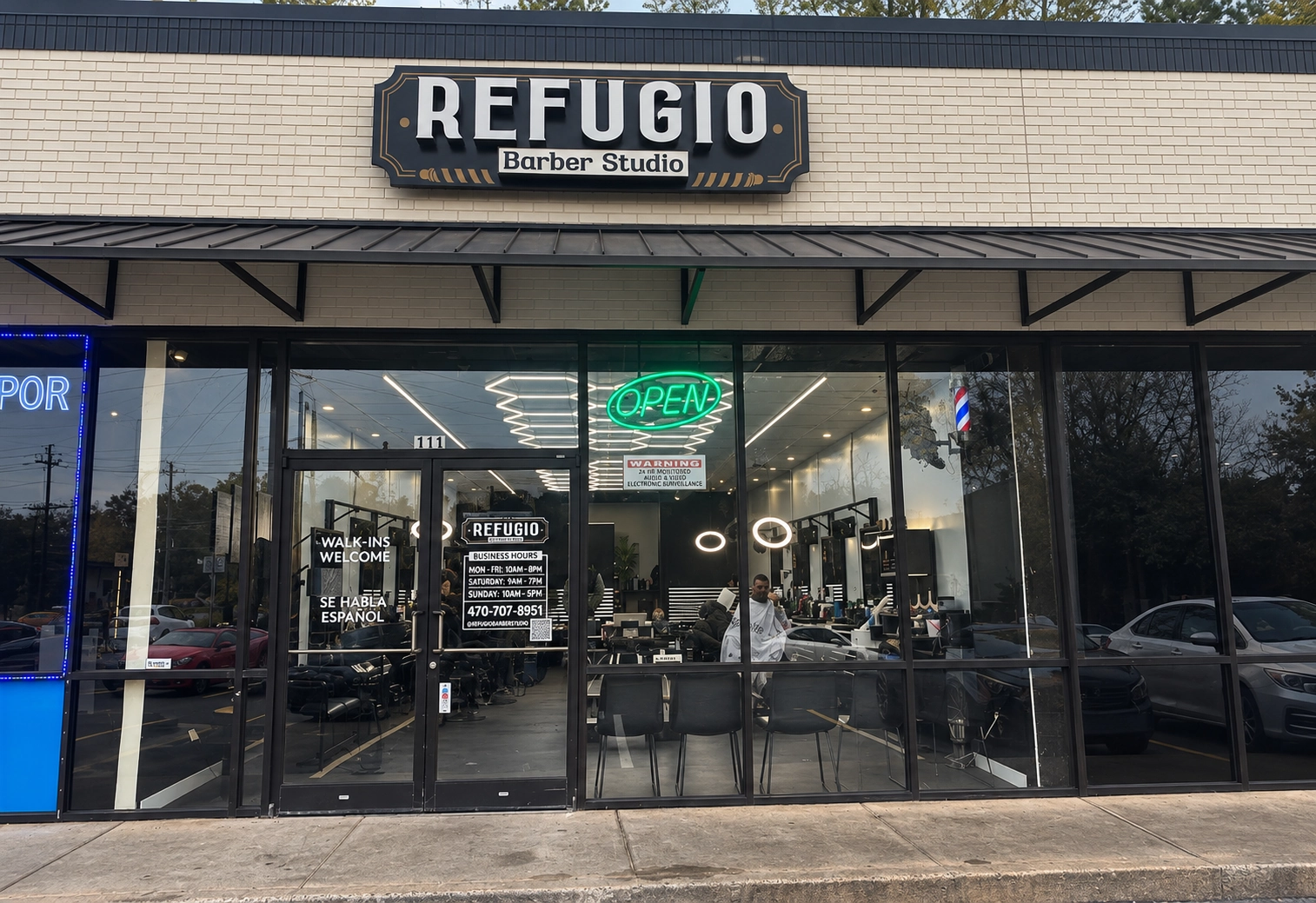 Refugio Barber Studio’s storefront at dusk, with the open sign lit